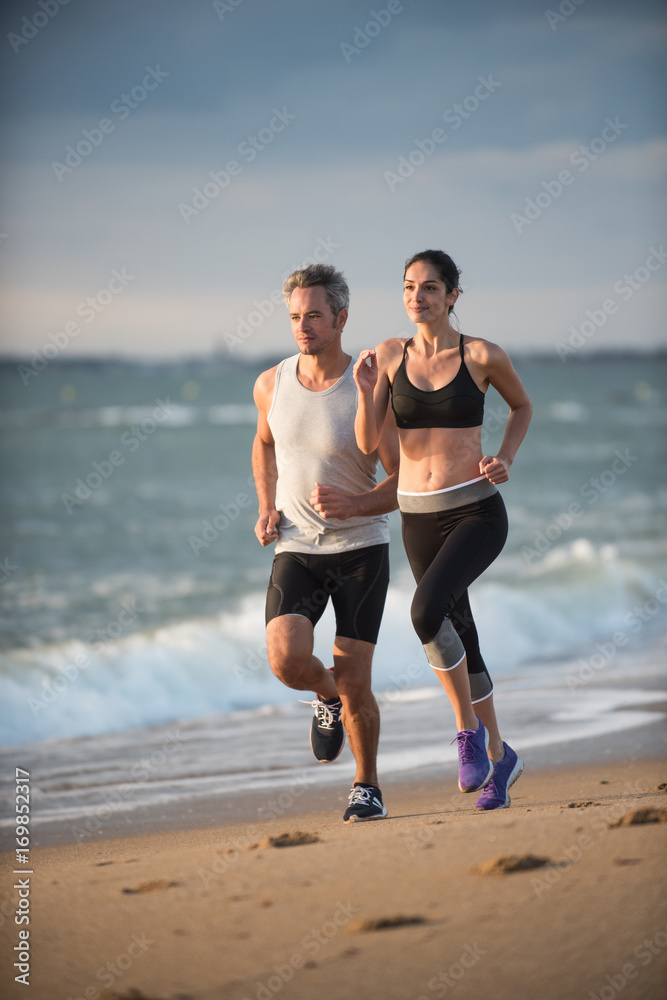 A couple wearing sportswear is running on the beach