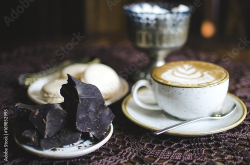 Coffee breack with chocolate and macaroons. Latte on retro brown wooden table with tablecloth photo