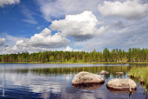 Lake landscape with a forest, stones and the beautiful sky with clouds on a summer day. Karelia, Russia.