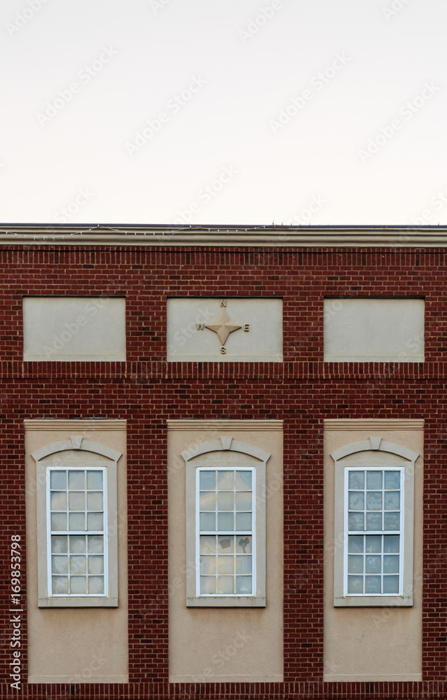 Historic brick facade of a building with three windows and decorative four pointed relief sculpture on the upper center part of the building