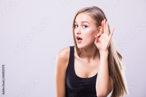 Close up Woman holds her hand near ear and listens carefully isolated on gray wall background. Human emotion body language facial face expression