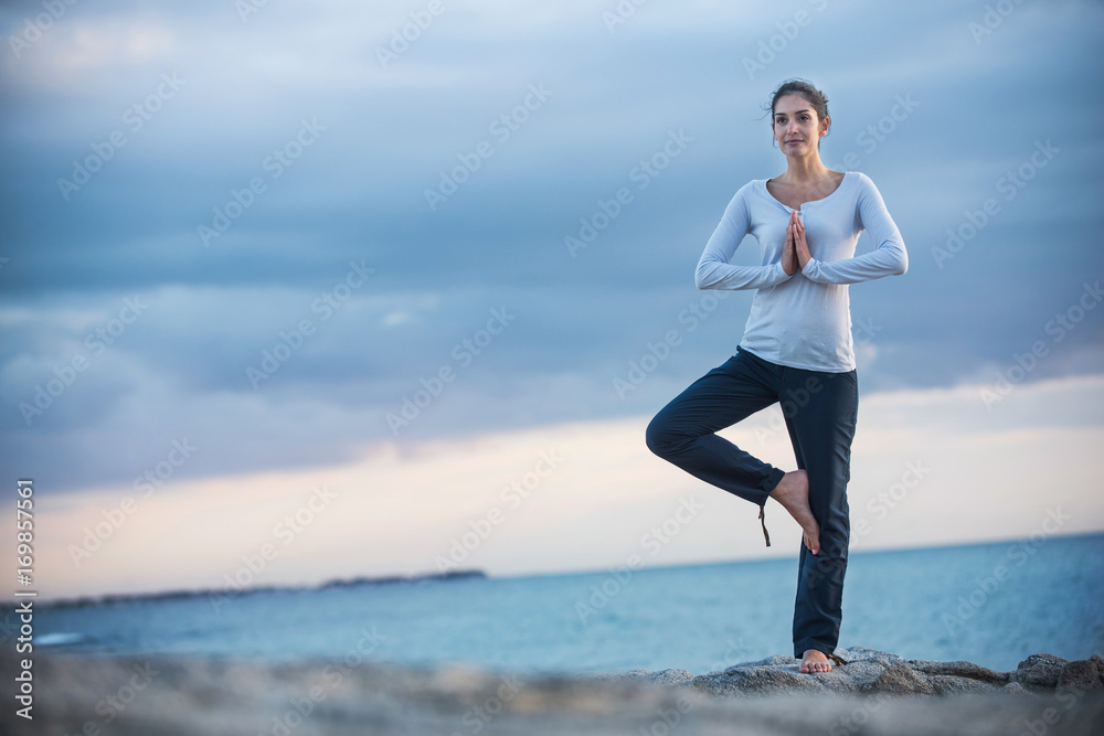 Beautiful woman practicing yoga on the beach at sunrise