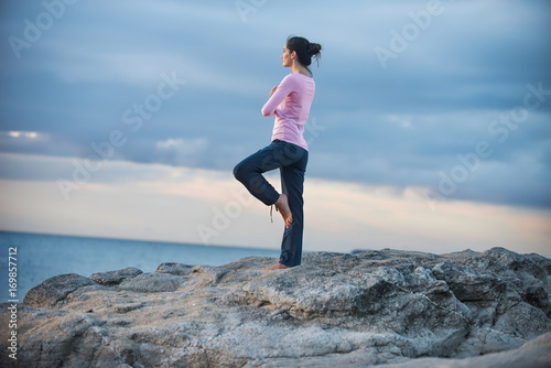 Beautiful woman practicing yoga on the beach at sunrise
