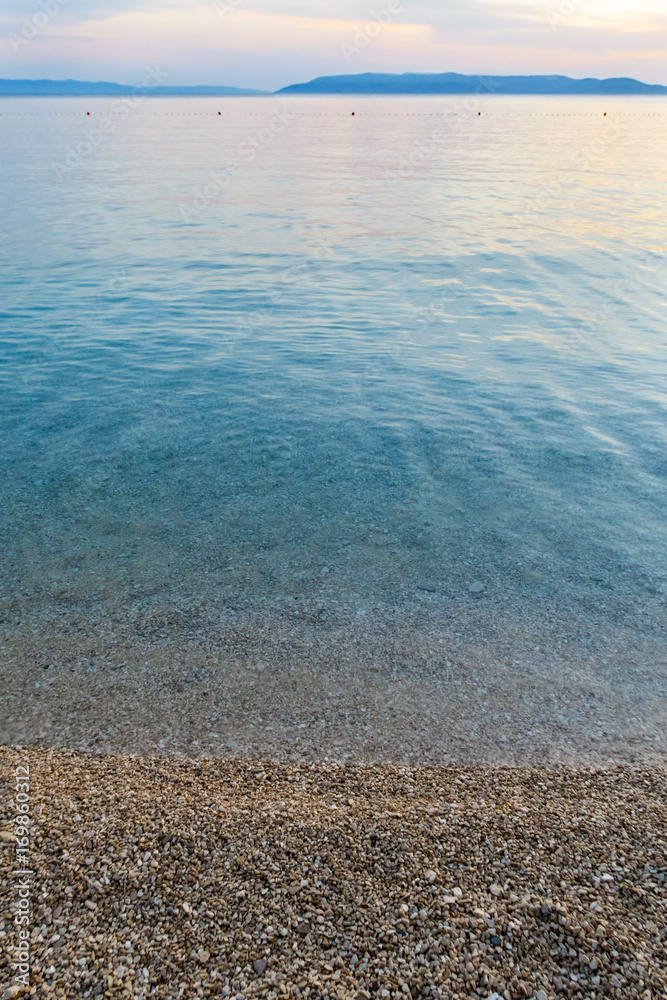 Calm clean sea with pebble beach and land on the horizon.