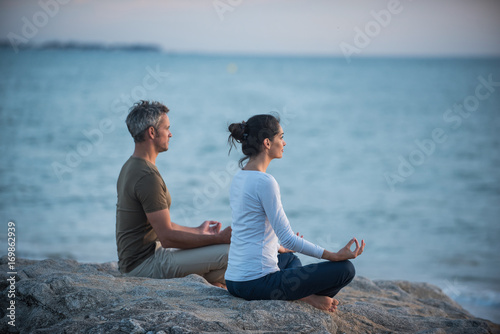Couple practicing yoga at sunrise on the beach facing the sea photo