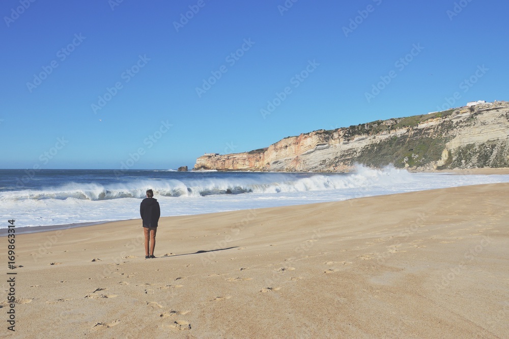 A man standing on a beach in Nazare, Portugal.