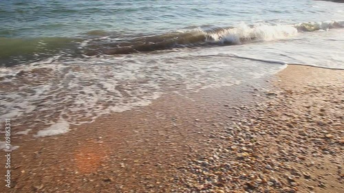 Wild stormy seashore with sand and pebbles on the beach, surf waves under morning sunlight.Tracking right.