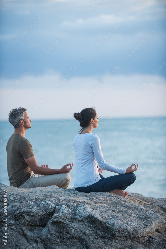 Couple practicing yoga at sunrise on the beach facing the sea Couple practicing yoga at sunrise on the beach facing the sea