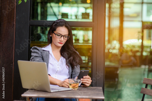 Young female freelancer checking email on cell during tea break with bokeh background. Business concept.