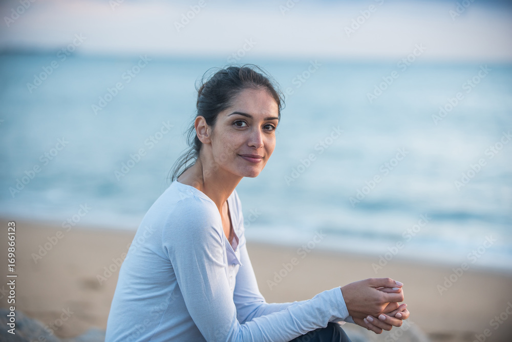 A beautiful young brunette sitting on a rock at the beach