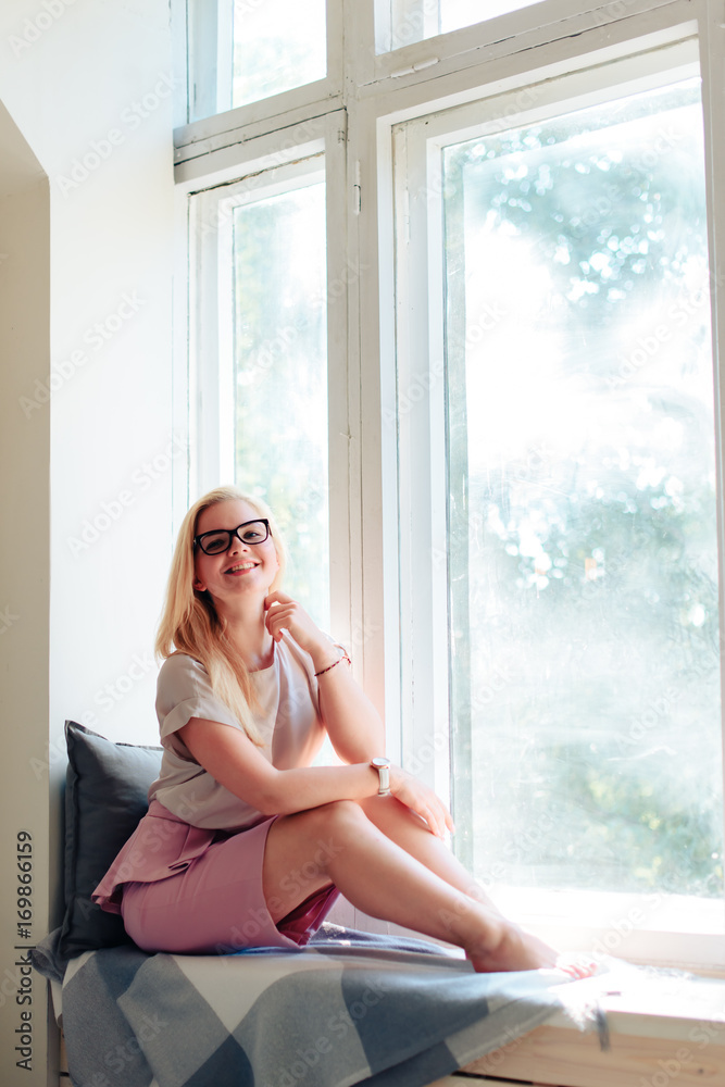 Beautiful young girl with glasses in a pink dress at the window