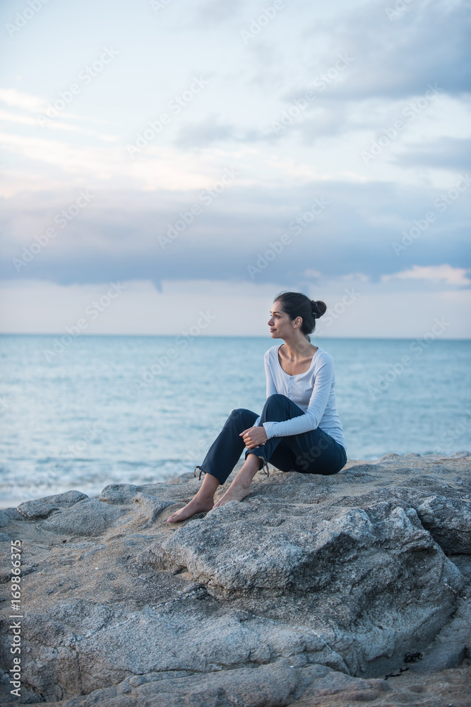 A beautiful young brunette sitting on a rock at the beach