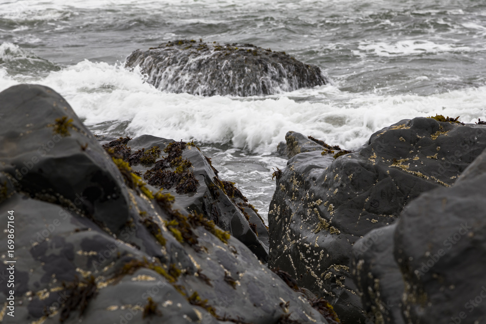 Obraz premium Waves crashing over black shoreline rocks at high tide