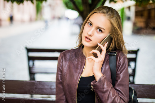 Happy girl calling on mobile phone sitting on a bench in the street photo
