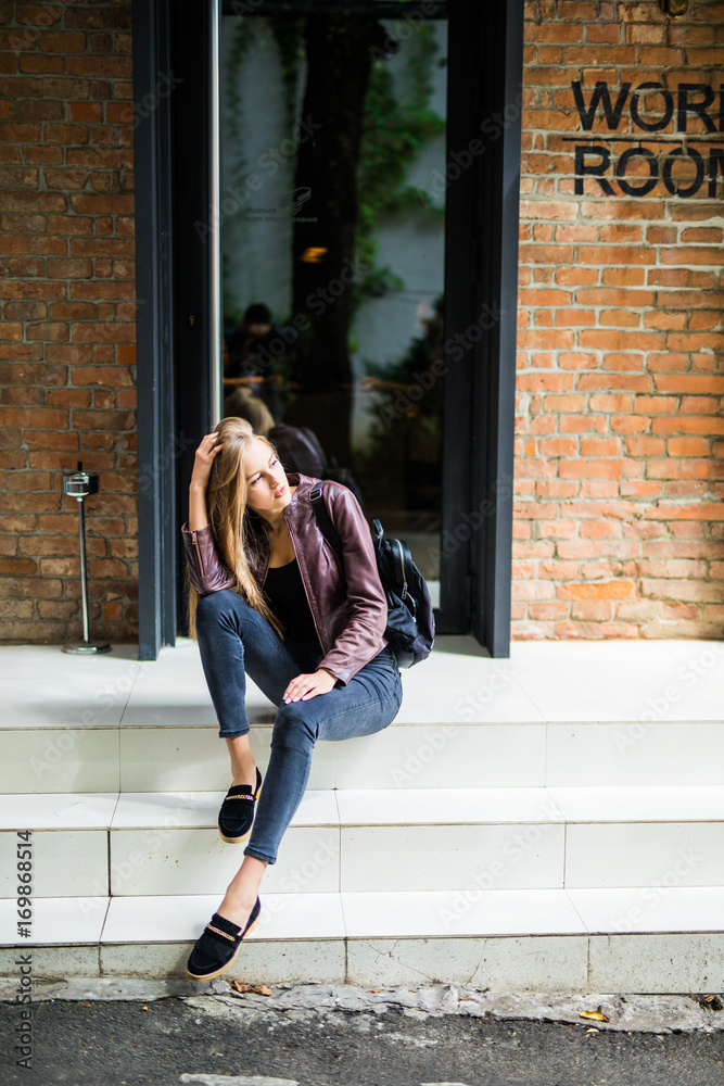 Casual style. Stylish woman in sunglasses sitting on the stone stairs. She dressed in jacket, skinny jeans and shoes. Long hair, elegant, street fashion Casual style. Stylish woman in sunglasses sitting on the stone stairs. She dressed in jacket, skinny jeans and shoes. Long hair, elegant, street fashion