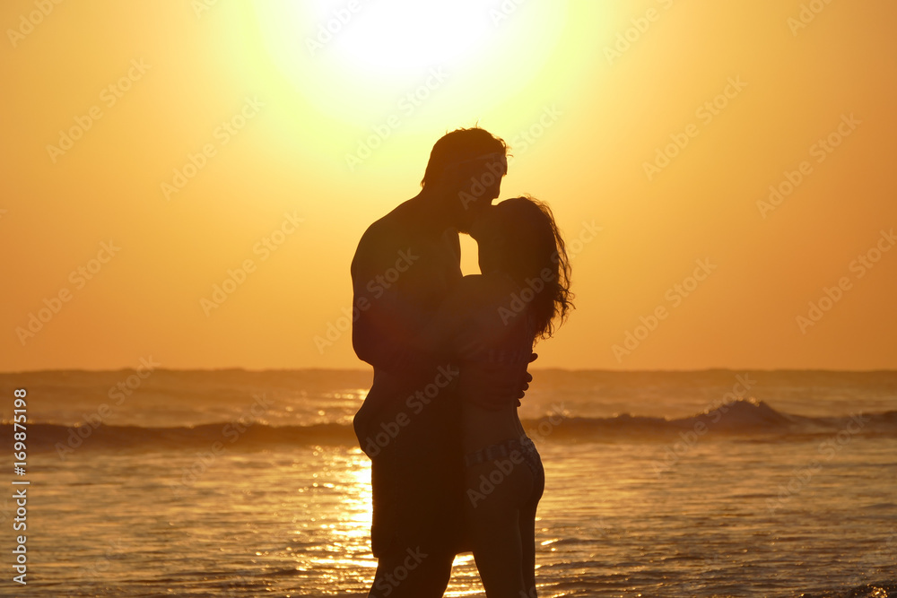 Aoung couple is kissing at beach during sunset