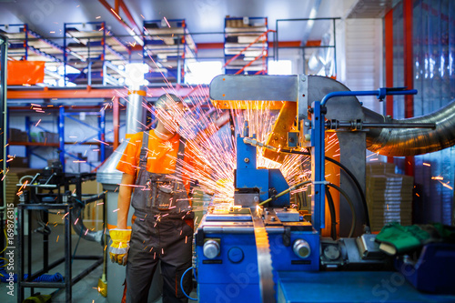 A male mechanic working on welding machine in the Industrial production of metal products. Sparks fly out of under the parts. Concept theme repair, mechanics, production, industry. Unrecognizable face