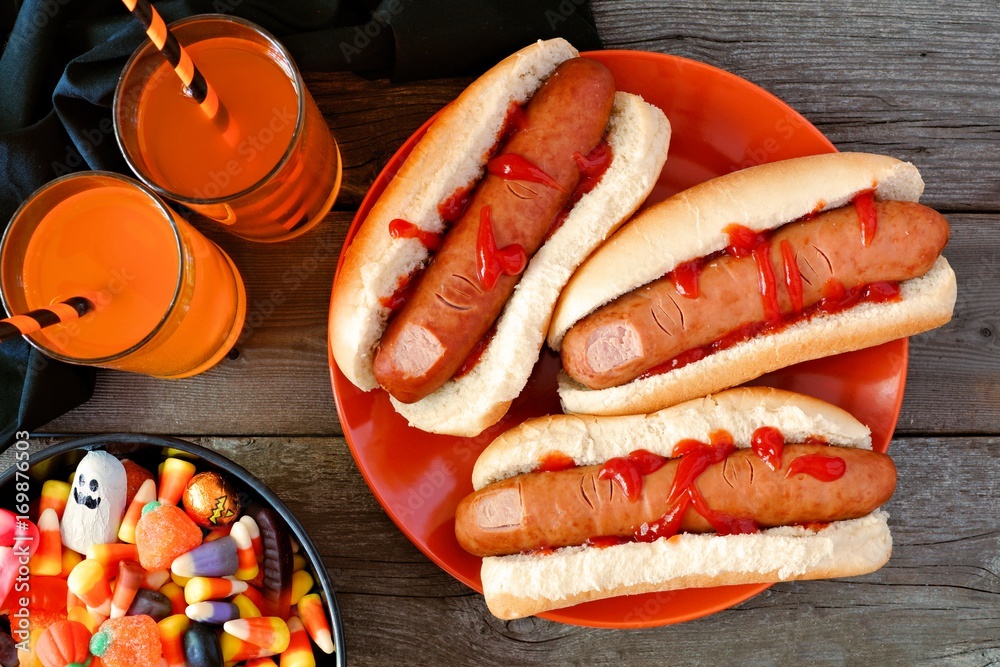 Obraz premium Halloween meal scene with hot dog fingers, drinks and candy, above view a wood background