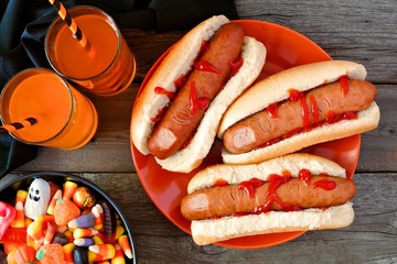 Halloween meal scene with hot dog fingers, drinks and candy, above view a wood background