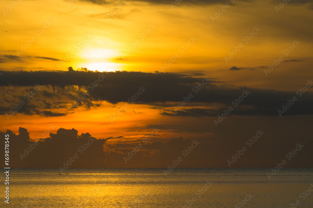 Fototapeta premium The sun shines through the clouds at dawn on the shore of the Gulf of Thailand.