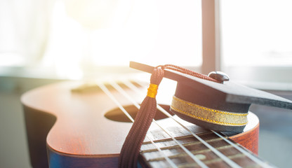 Graduation cap Put on ukulele, a small instrument. The ukulele is member of lute family of instruments with nylon stringed, usually played with bare thumb or fingertips. Concept of Music Education.