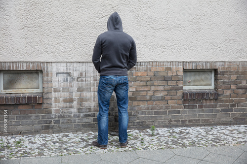 Obraz na plátne Man In Hood Peeing On Wall