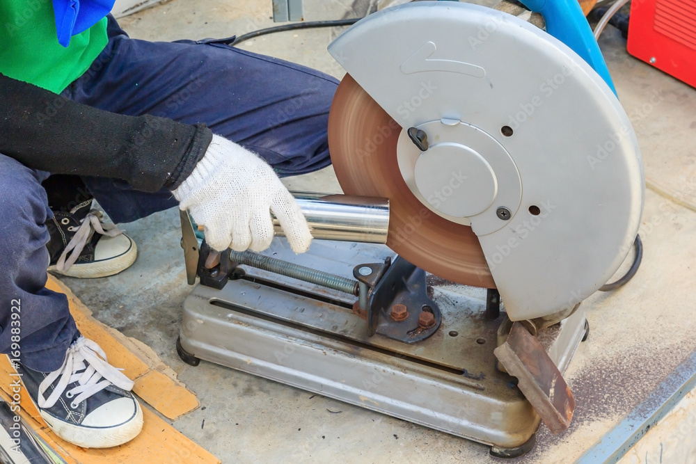 Industrial worker cutting metal with many sharp sparks working on compound mitre saw with circular blade