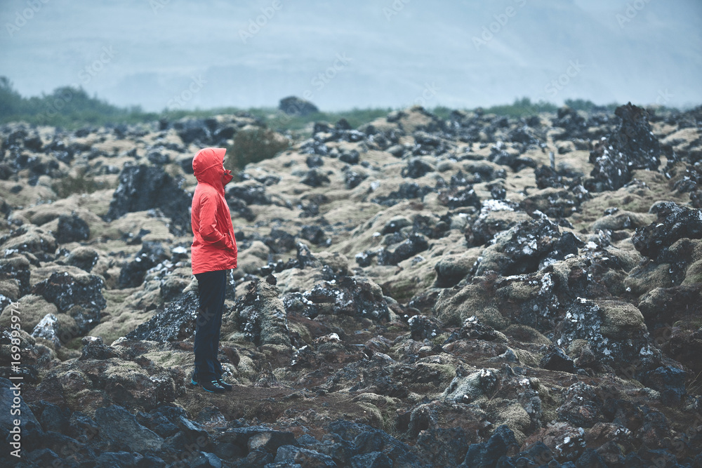 Obraz premium Woman in waterproof clothing walks on volcanic Lava fields on background of mountains of Iceland.