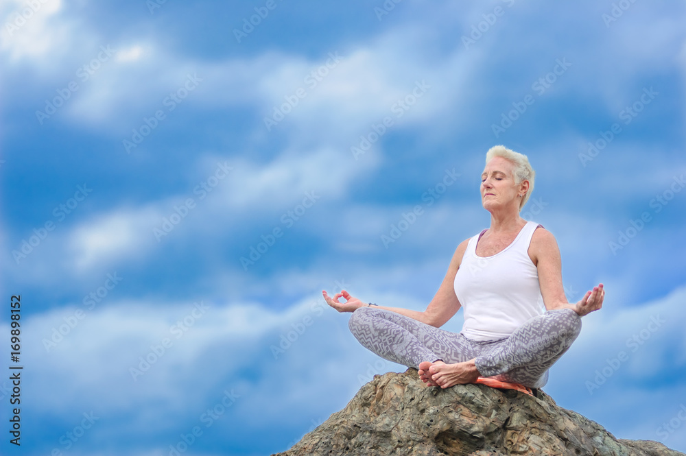Beautiful mature aged woman sits on top of a cliff doing yoga Beautiful mature aged woman sits on top of a cliff doing yoga