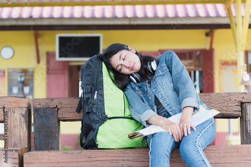 Asian tourist girl tired and sleep on the backpacks while waiting for the train at the local station.The concept of freedom and  travel.