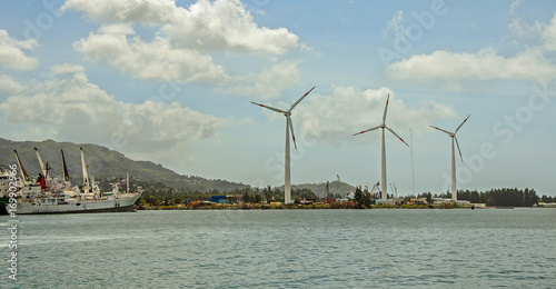 A waterfront with three wind turbines and a fishing ship near the green hills, Seychelles
