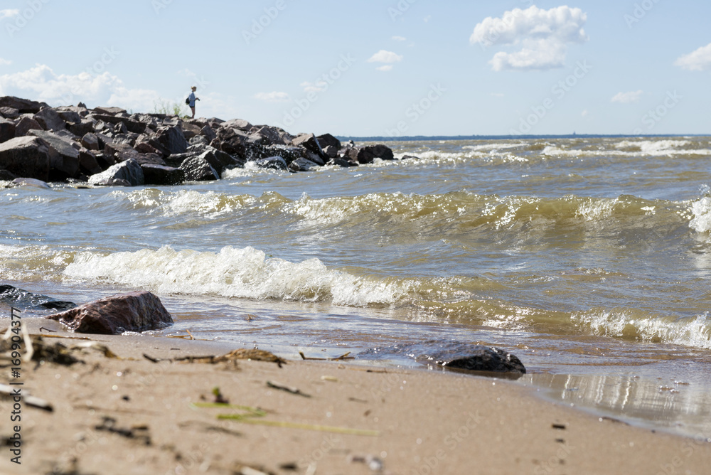 ocean waves lapping on the sandy shore, away girl standing on the rocks