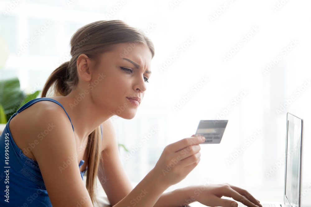 Beautiful serious young woman holding credit card in hand, attentively reading it number, typing on laptop, making purchases in Internet. Pretty lady using online banking service for sending payments Beautiful serious young woman holding credit card in hand, attentively reading it number, typing on laptop, making purchases in Internet. Pretty lady using online banking service for sending payments