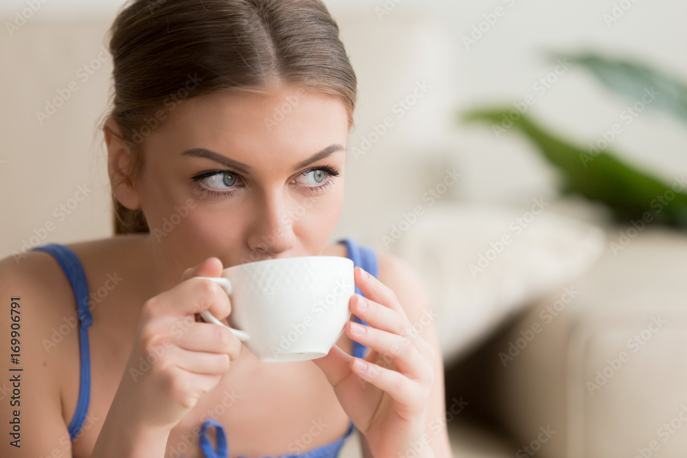 Headshot portrait of young woman with porcelain white cup in hands drinking coffee, looking in window after wake up. Pretty lady enjoying fresh brewed invigorating drink with caffeine relaxing in cafe Headshot portrait of young woman with porcelain white cup in hands drinking coffee, looking in window after wake up. Pretty lady enjoying fresh brewed invigorating drink with caffeine relaxing in cafe