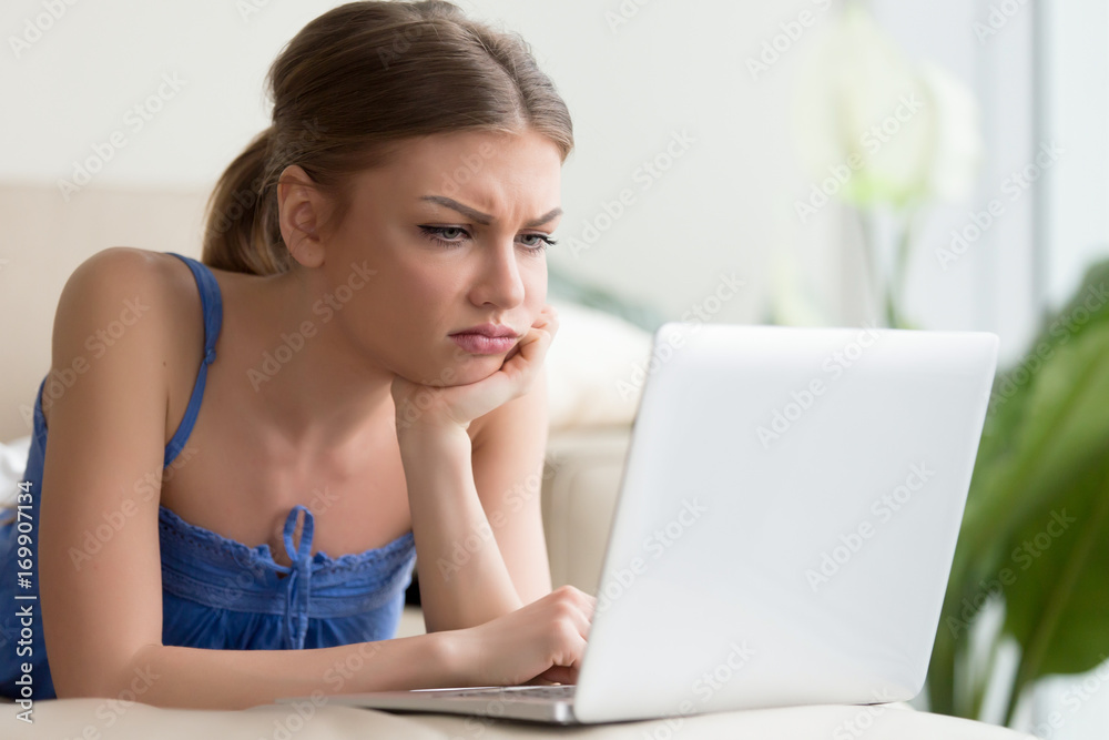 Dissatisfied young woman with grumpy face and head resting on hand looking on laptop screen. Annoyed millennial lady browsing social network, watching boring movie, tired because of too long searching Dissatisfied young woman with grumpy face and head resting on hand looking on laptop screen. Annoyed millennial lady browsing social network, watching boring movie, tired because of too long searching
