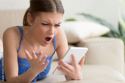 Bilde på lerret Young woman feeling shocked and looking with confusion on digital tablet screen while browsing online at home