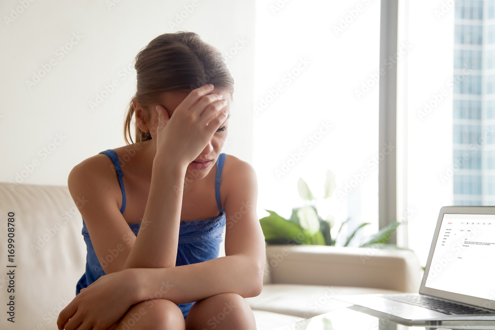 Stressed young woman in casual clothes sitting upset on sofa in front of laptop. Worried lady frustrated because of bad news in e-mail letter or message opened on computer screen, shocked of dismissal Stressed young woman in casual clothes sitting upset on sofa in front of laptop. Worried lady frustrated because of bad news in e-mail letter or message opened on computer screen, shocked of dismissal