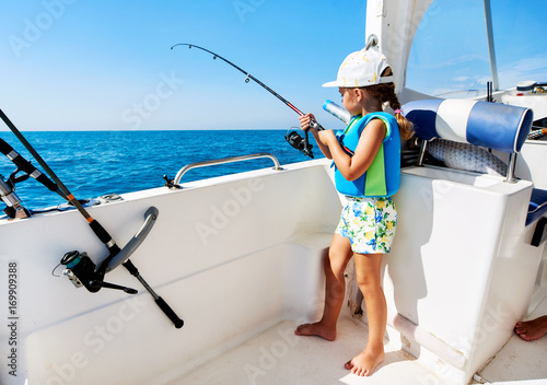 Fototapeta Little girl with a fishing rod fishing from the boat