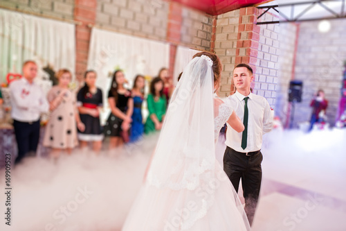 Wedding couple dancing their first wedding dance with heavy smoke and different lights in the restaurant full of guests.