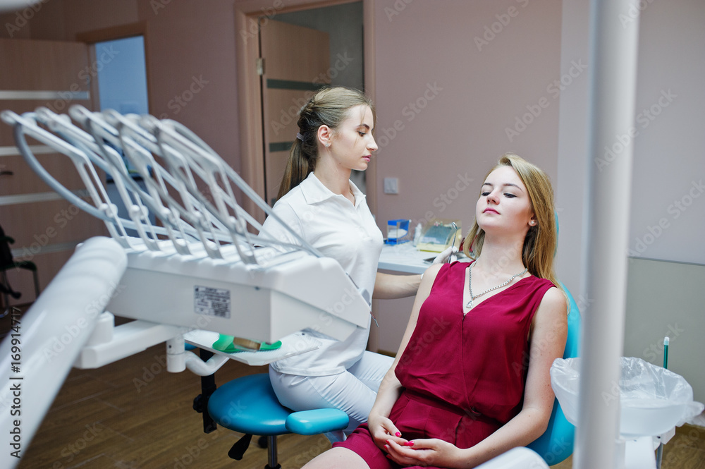 Beuatiful female dentist posing and smiling with her lovely patient laying on a dental chair in red-violet dress. Beuatiful female dentist posing and smiling with her lovely patient laying on a dental chair in red-violet dress.