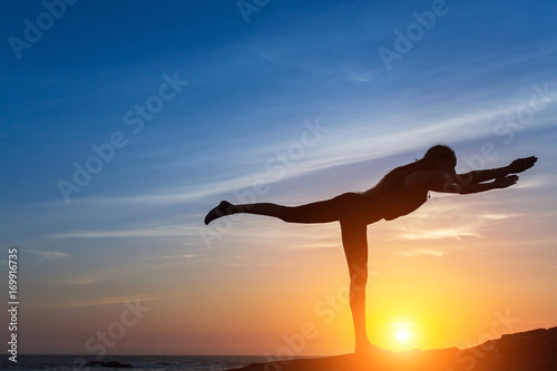 Fototapeta Naklejka Na Ścianę i Meble -  Woman silhouette doing fitness exercise on the sea beach during sunset.