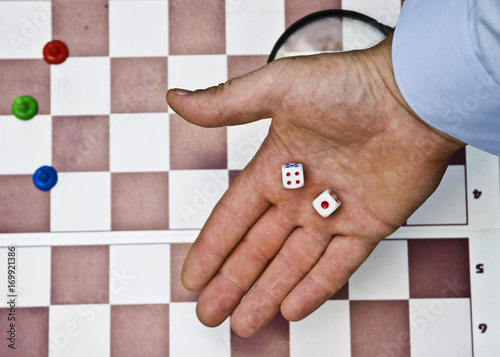 Dice in the male palm on the background of a chessboard with playing pawns