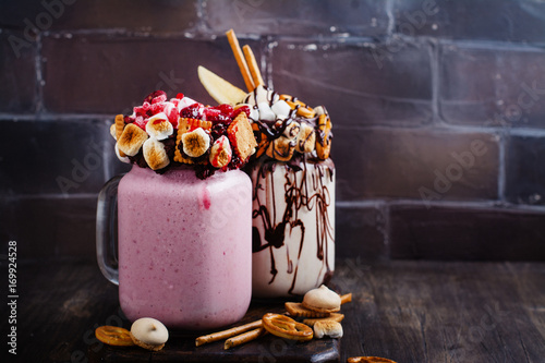 Vanilla and raspberry extreme milkshakes with bretzels, popcorn, small marshmallows, cookies and berries on white background. Copy space photo