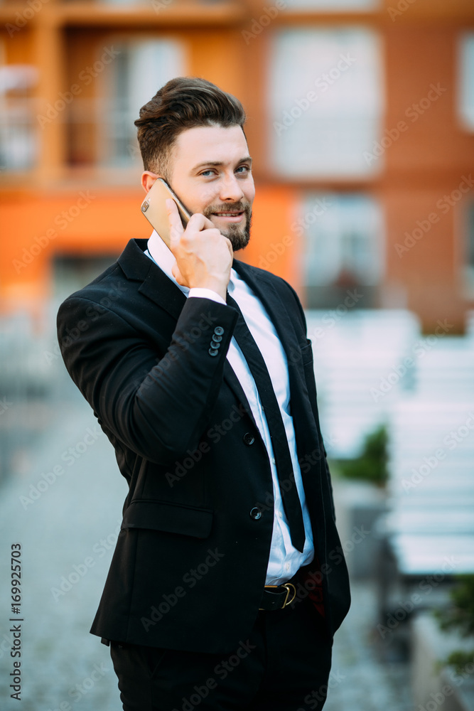 Handsome young businessman walking on the street and talking on his phone Handsome young businessman walking on the street and talking on his phone