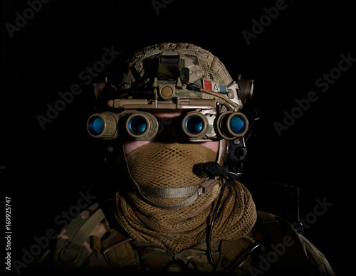 Fotografie Soldier in military uniform with night vision goggles on background of dark wall