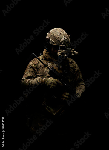 Soldier in military uniform with assault rifle standing on background of dark wall 20