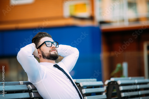 Relaxed business man sitting on a bench with hands over head and enjoy free time after success #169926992