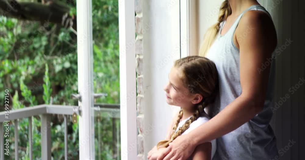 Mother and daughter looking through window in bedroom Mother and daughter looking through window in bedroom