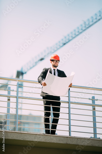 Handsome man Engineering Consulting people on construction site holding blueprint in his hand. Building inspector. Construction site check drawing and business workflow of new building photo