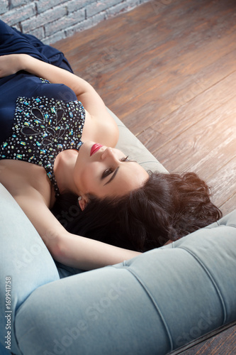 Fashion photo of beautiful lady in elegant evening dress with bright makeup with red lips and hairstyling in minimalist loft interior.
